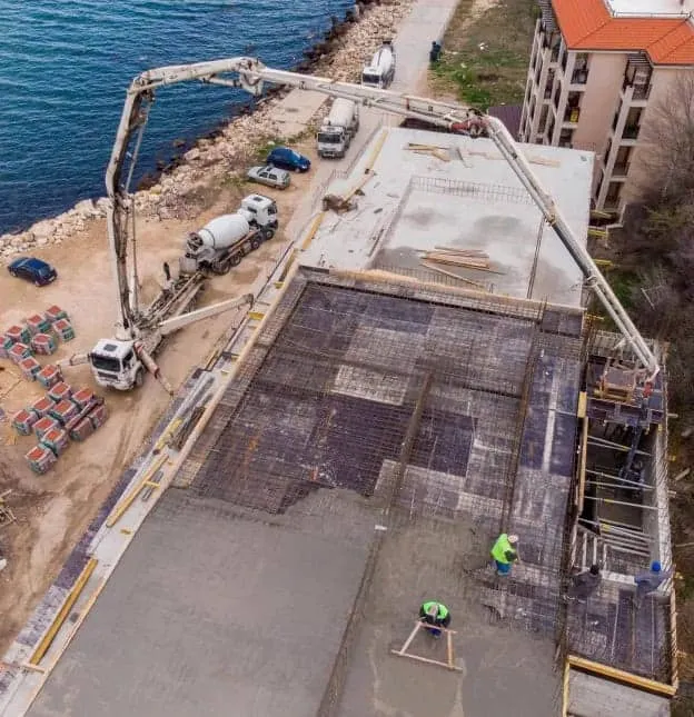 Truck-mounted concrete pump placing a slab, with mixer trucks queued on the access road